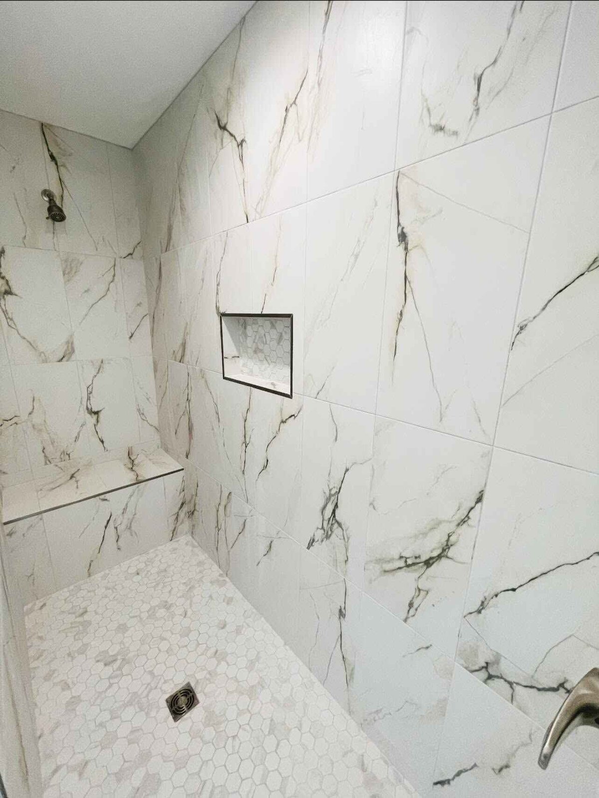 Luxury bathroom shower enclosure with white marble-veined tile walls and hexagonal tile floor with drain