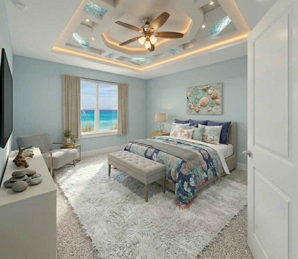 Modern bedroom with light blue walls, ocean view window, ceiling fan, queen bed with blue patterned bedding, and neutral carpet