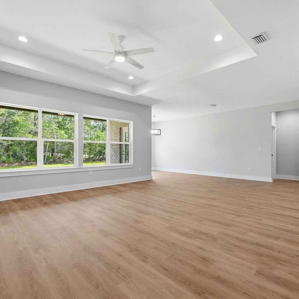 Empty modern room with hardwood floors, large windows overlooking greenery, white walls, ceiling fan, and recessed lighting