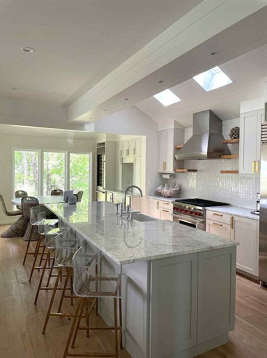 Modern kitchen with light green island, white cabinetry, marble countertops, skylight, and seating area overlooking garden